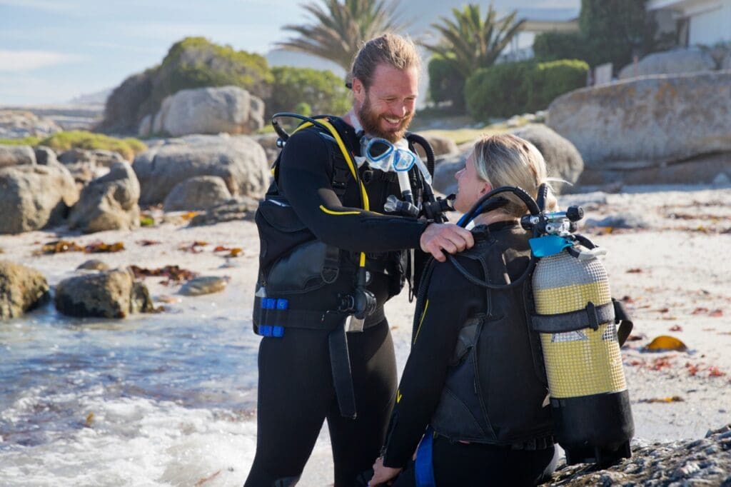 Divemaster helping a scuba diver with her equipment before entering the water