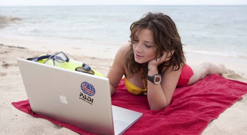 Divemaster searching online for scuba diving jobs from a tropical beach